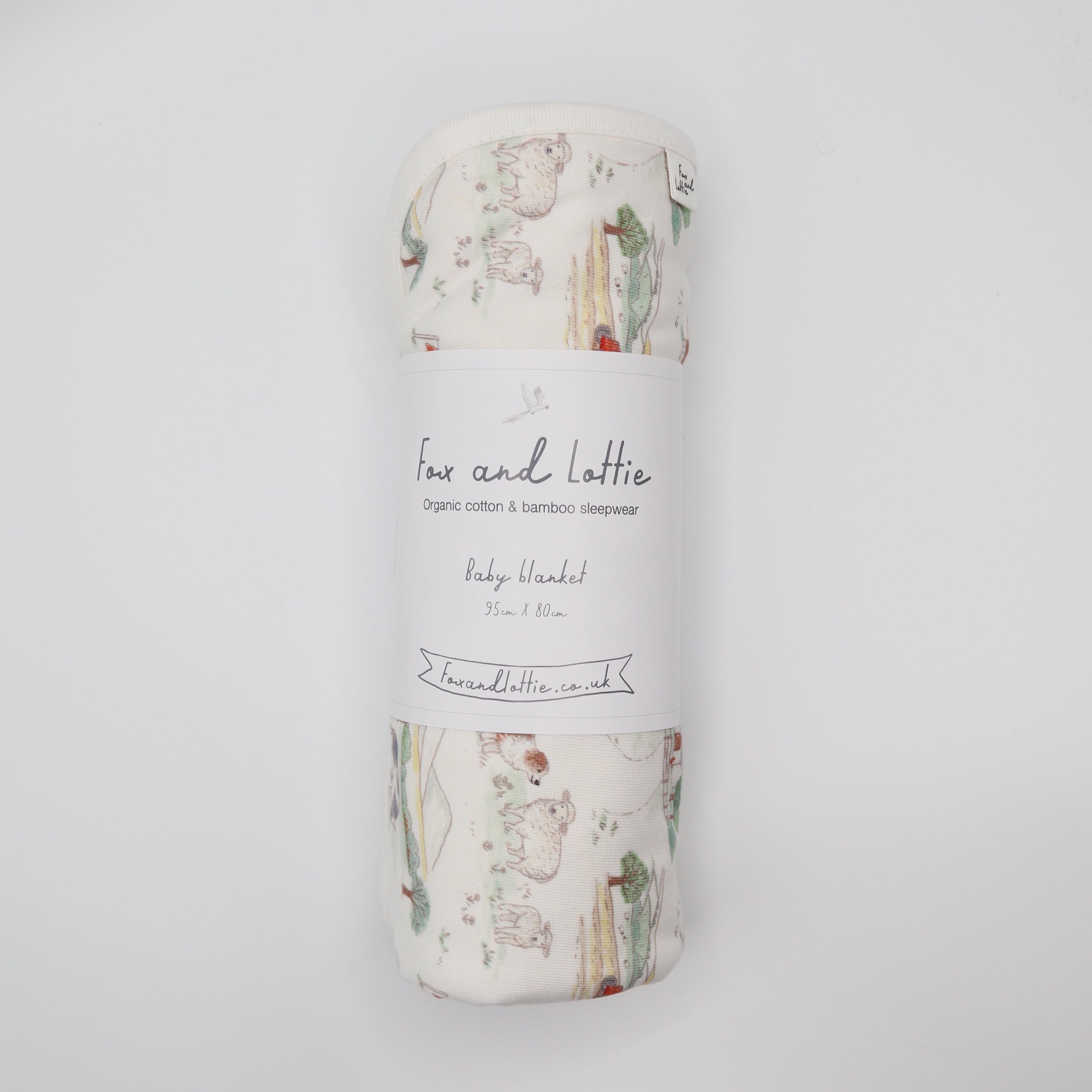 Rolled-up baby blanket with 'Fox and Lottie' branding on a light gray background. Farm blanket