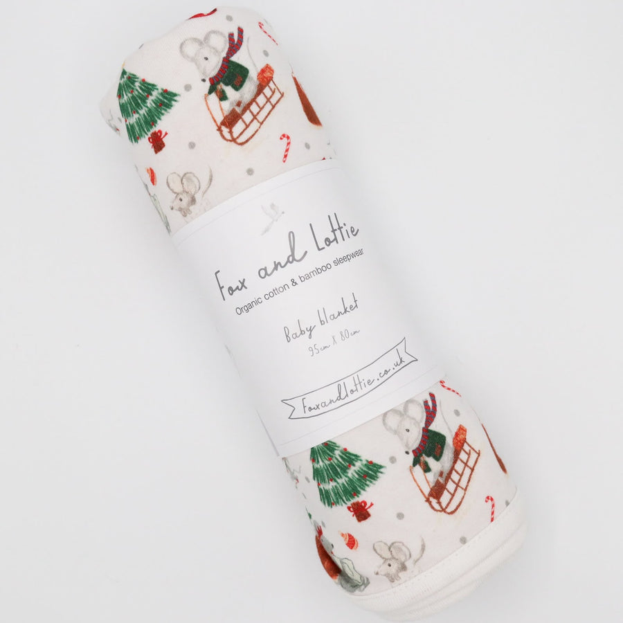 A rolled baby blanket with a festive Christmas print featuring a mouse in a sled. Premium sleepwear by Fox and Lottie.